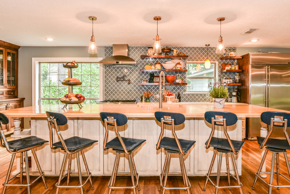 Inspiration for a single-wall medium tone wood floor and beige floor eat-in kitchen remodel in Houston with a drop-in sink, recessed-panel cabinets, distressed cabinets, wood countertops, blue backsplash, glass tile backsplash, stainless steel appliances and an island