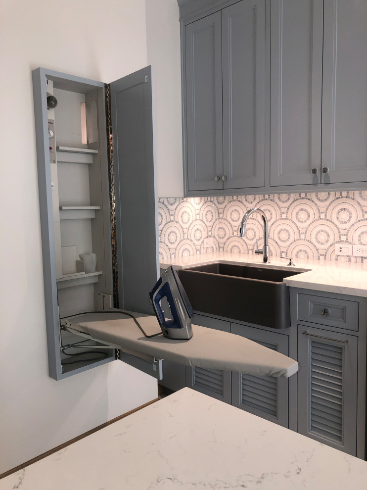 Design ideas for a large transitional u-shaped dedicated laundry room in San Diego with a farmhouse sink, shaker cabinets, blue cabinets, quartz benchtops, blue splashback, mosaic tile splashback, white walls, porcelain floors, a side-by-side washer and dryer, grey floor and white benchtop.