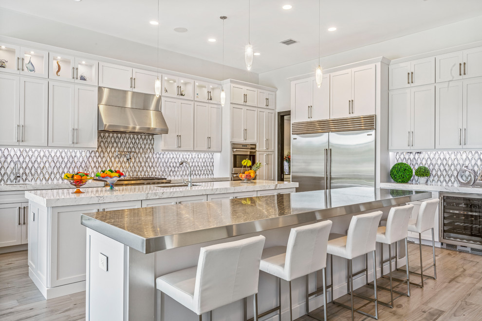 Photo of a mid-sized transitional u-shaped kitchen in Miami with an undermount sink, shaker cabinets, white cabinets, stainless steel appliances, medium hardwood floors, multiple islands, brown floor, marble benchtops, multi-coloured splashback, mosaic tile splashback and white benchtop.