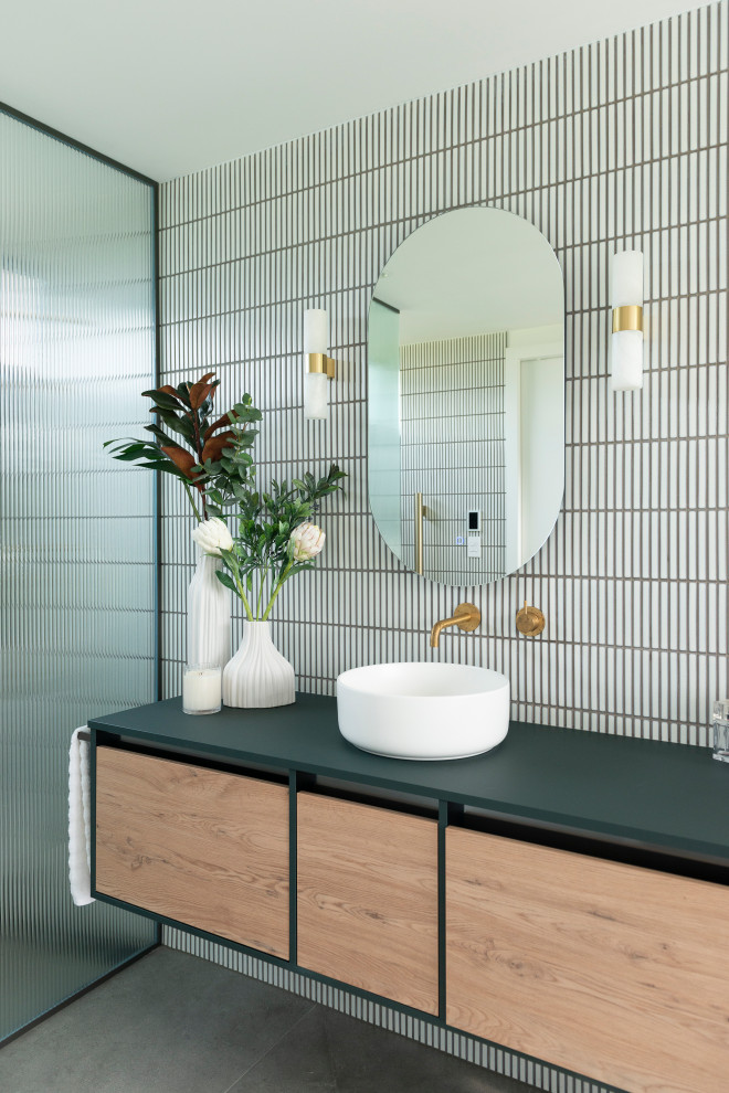 Photo of a mid-sized beach style master bathroom in Auckland with flat-panel cabinets, green cabinets, a freestanding tub, a curbless shower, a one-piece toilet, white tile, porcelain tile, white walls, porcelain floors, a vessel sink, solid surface benchtops, grey floor, an open shower, white benchtops, a niche, a single vanity and a floating vanity.