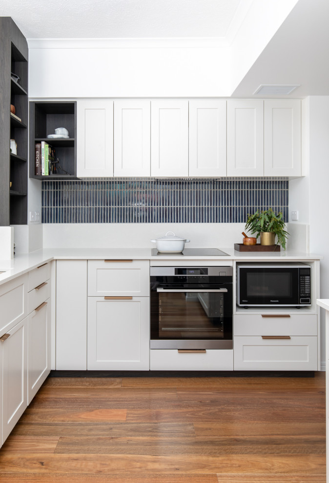 Klassische Küche in L-Form mit Schrankfronten im Shaker-Stil, weißen Schränken, Quarzwerkstein-Arbeitsplatte, Küchenrückwand in Blau, Rückwand aus Porzellanfliesen, braunem Boden und weißer Arbeitsplatte in Brisbane