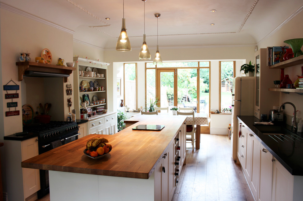 Photo of a mid-sized country u-shaped eat-in kitchen in Other with a drop-in sink, recessed-panel cabinets, white cabinets, wood benchtops, white splashback, black appliances, medium hardwood floors and with island.