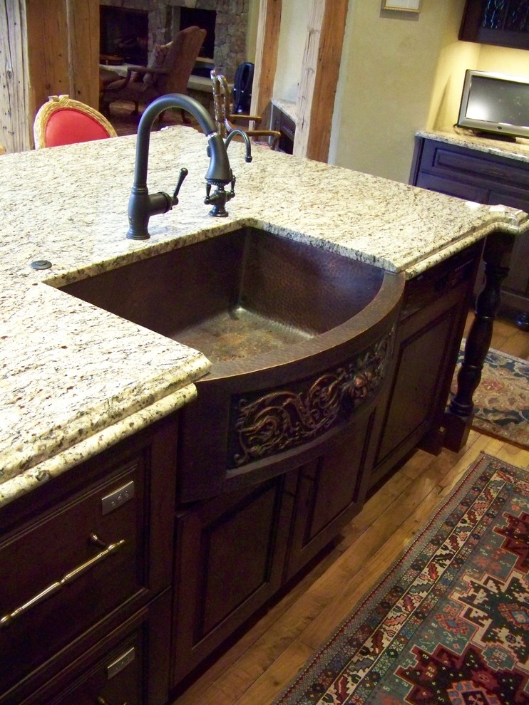 This is an example of a mid-sized country l-shaped eat-in kitchen in Denver with a farmhouse sink, beaded inset cabinets, dark wood cabinets, granite benchtops, light hardwood floors and with island.