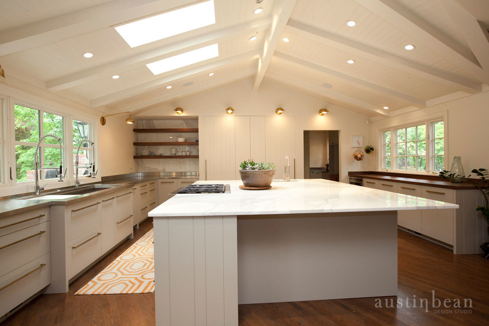 Large transitional u-shaped medium tone wood floor eat-in kitchen photo with an integrated sink, flat-panel cabinets, white cabinets, stainless steel countertops, white backsplash, stone slab backsplash, stainless steel appliances and white walls