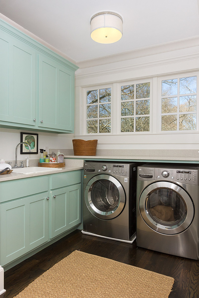 Photo of a mid-sized transitional l-shaped dedicated laundry room in Atlanta with blue cabinets, a drop-in sink, brown floor, shaker cabinets, white walls, dark hardwood floors, a side-by-side washer and dryer and beige benchtop.