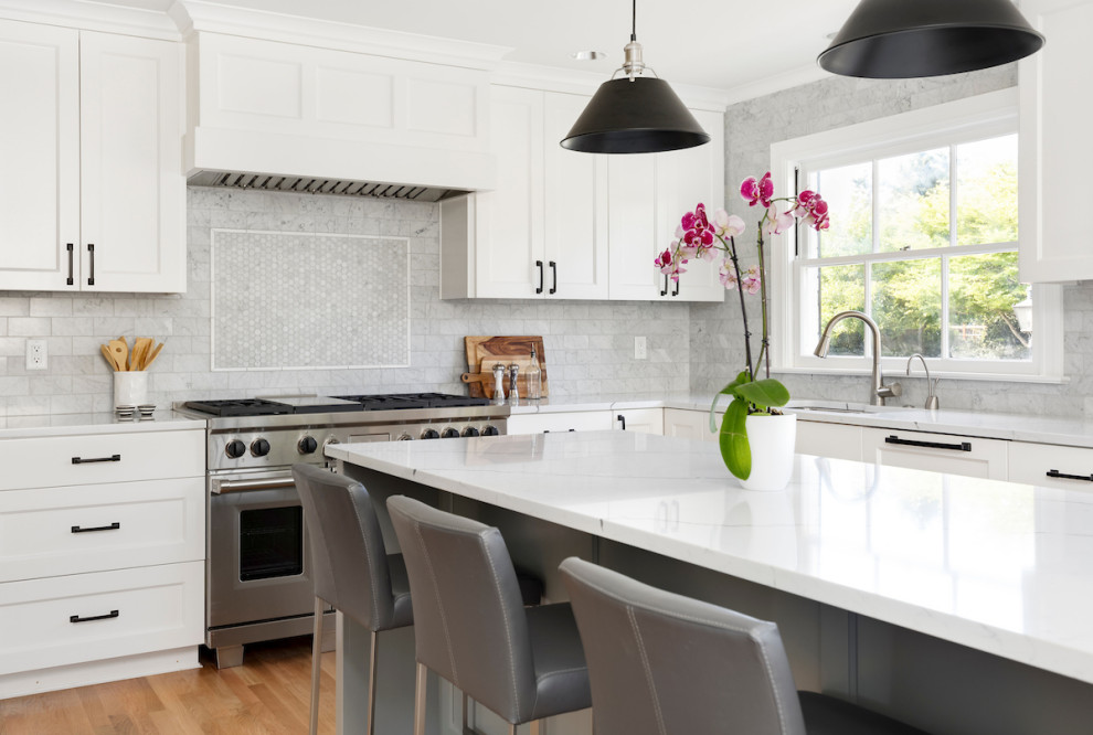 Inspiration for a large transitional l-shaped kitchen in Portland with shaker cabinets, white cabinets, quartz benchtops, grey splashback, glass tile splashback, stainless steel appliances, light hardwood floors, with island, brown floor, white benchtop and an undermount sink.