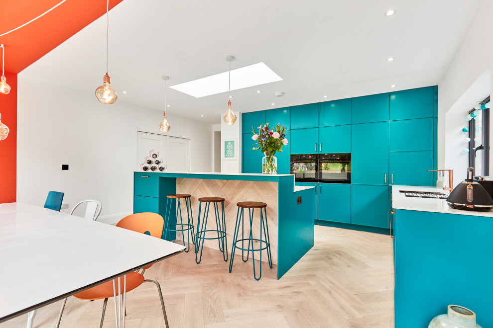 This is an example of a medium sized contemporary l-shaped kitchen/diner in Other with a built-in sink, recessed-panel cabinets, blue cabinets, quartz worktops, white splashback, black appliances, laminate floors, an island, beige floors, white worktops, a vaulted ceiling and a feature wall.