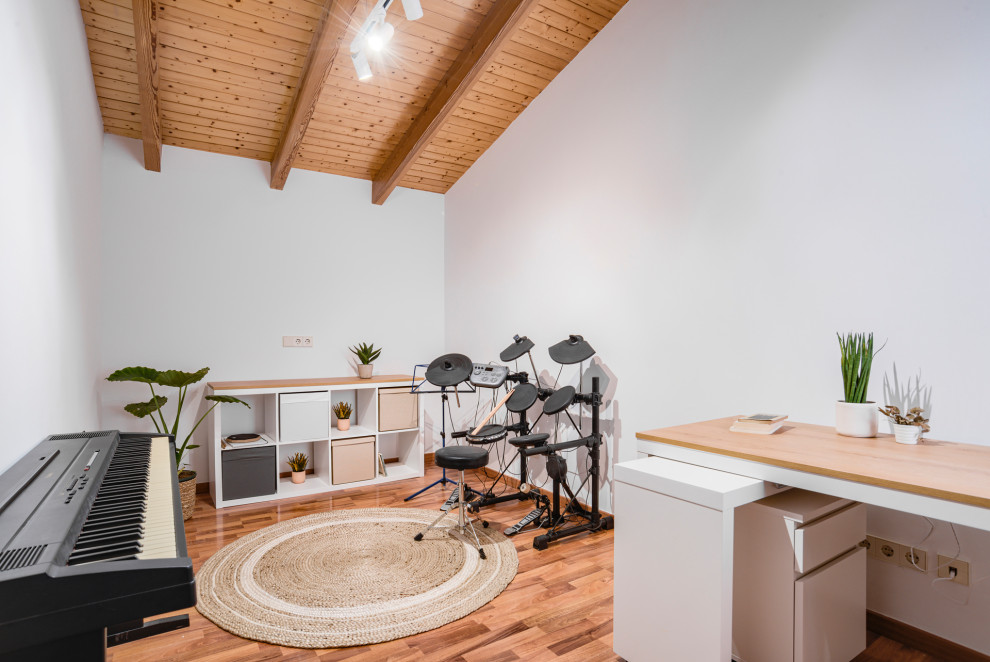 Mittelgroßes Skandinavisches Arbeitszimmer mit Studio, weißer Wandfarbe, braunem Holzboden, freistehendem Schreibtisch und freigelegten Dachbalken in Barcelona