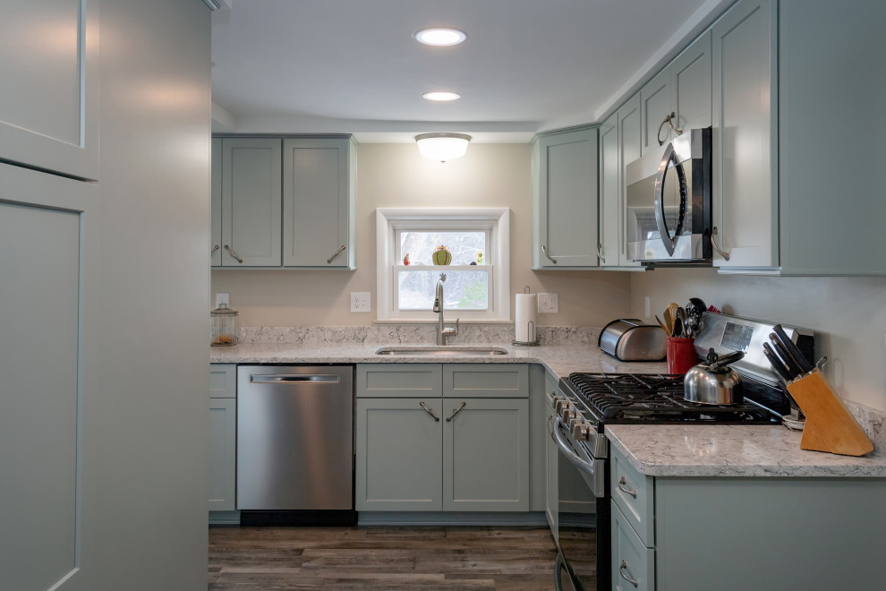 Small transitional l-shaped vinyl floor and brown floor enclosed kitchen photo with an undermount sink, shaker cabinets, green cabinets, quartz countertops, stainless steel appliances, a peninsula and gray countertops