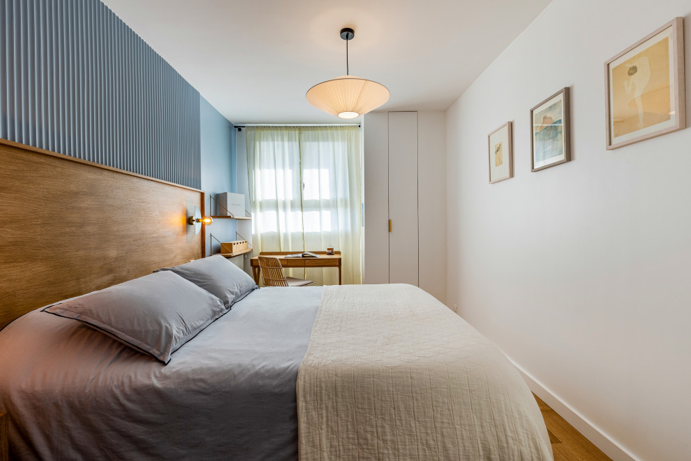 This is an example of a mid-sized midcentury master bedroom in Paris with blue walls, light hardwood floors, no fireplace, brown floor and decorative wall panelling.