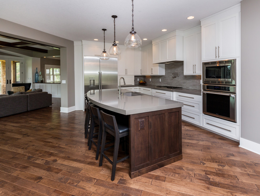 Inspiration for a large transitional l-shaped dark wood floor eat-in kitchen remodel with an undermount sink, shaker cabinets, white cabinets, solid surface countertops, gray backsplash, stainless steel appliances and an island