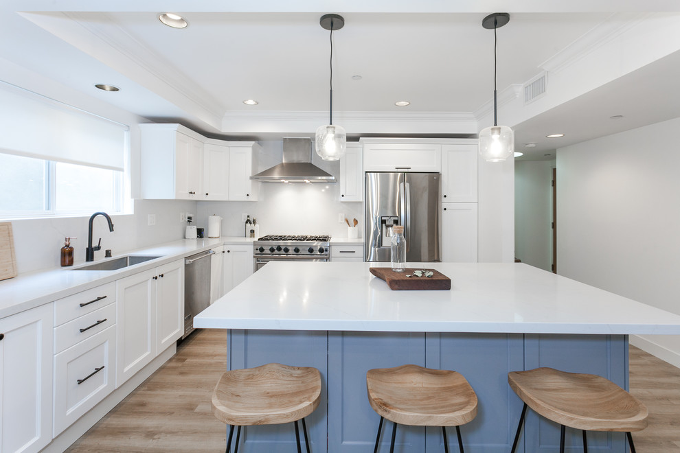 Photo of a mid-sized modern l-shaped eat-in kitchen in Los Angeles with an undermount sink, beaded inset cabinets, white cabinets, quartz benchtops, white splashback, porcelain splashback, stainless steel appliances, vinyl floors, with island, brown floor and white benchtop.