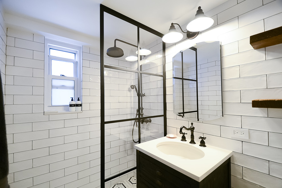 Photo of a mid-sized industrial bathroom in New York with furniture-like cabinets, brown cabinets, a double shower, a one-piece toilet, white tile, subway tile, white walls, porcelain floors, a pedestal sink, brown floor, an open shower and white benchtops.