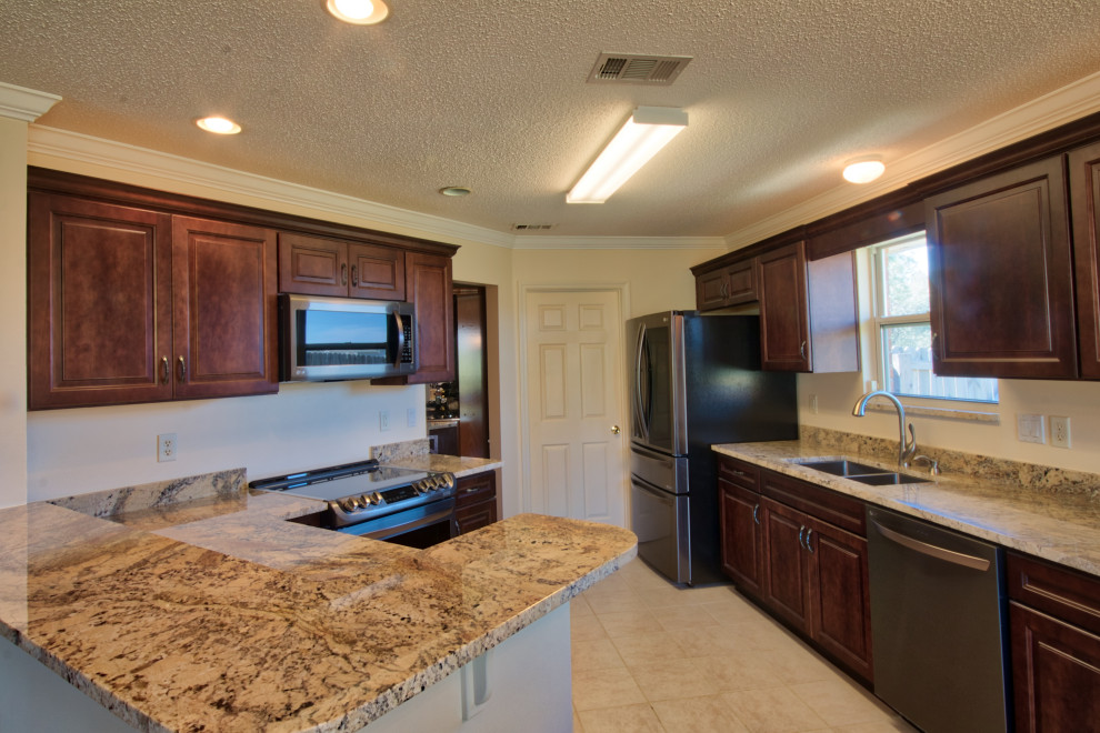 Foto på ett mellanstort beige kök, med en undermonterad diskho, luckor med upphöjd panel, skåp i mörkt trä, granitbänkskiva, rostfria vitvaror, cementgolv, en halv köksö och rosa golv