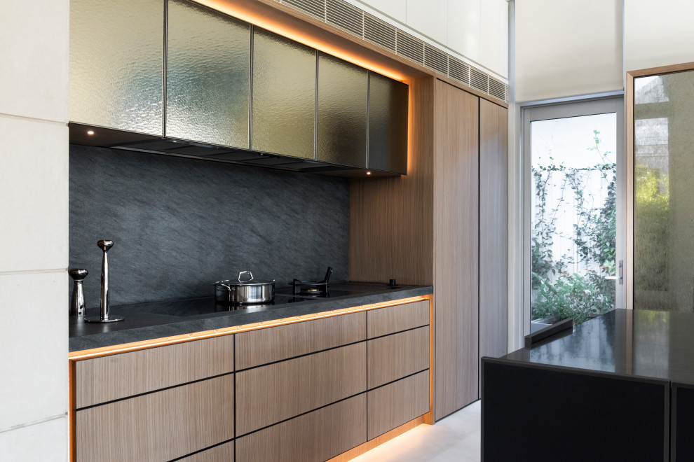 This is an example of a large modern galley open plan kitchen in Sydney with a drop-in sink, flat-panel cabinets, medium wood cabinets, quartz benchtops, black splashback, marble splashback, stainless steel appliances, ceramic floors, with island, white floor and black benchtop.