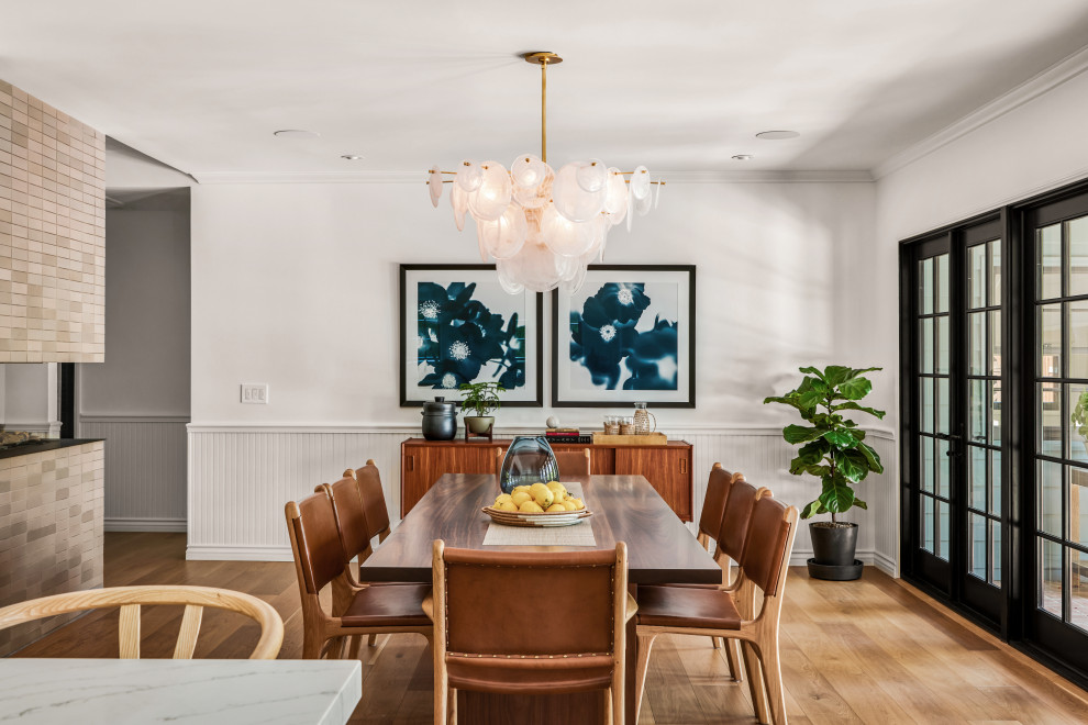 This is an example of a medium sized scandi enclosed dining room in Los Angeles with white walls, medium hardwood flooring, a two-sided fireplace, a tiled fireplace surround, beige floors, wainscoting and feature lighting.
