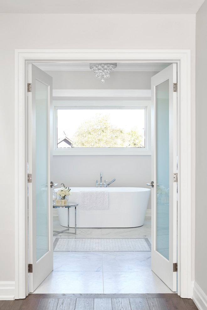 Inspiration for a mid-sized transitional master gray tile and ceramic tile white floor freestanding bathtub remodel with shaker cabinets, gray cabinets, a two-piece toilet, gray walls, an undermount sink, solid surface countertops and a hinged shower door