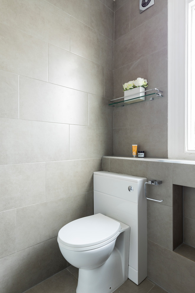 This is an example of a small contemporary 3/4 bathroom in London with open cabinets, beige cabinets, a curbless shower, a one-piece toilet, beige tile, stone tile, beige walls, ceramic floors, a wall-mount sink and tile benchtops.
