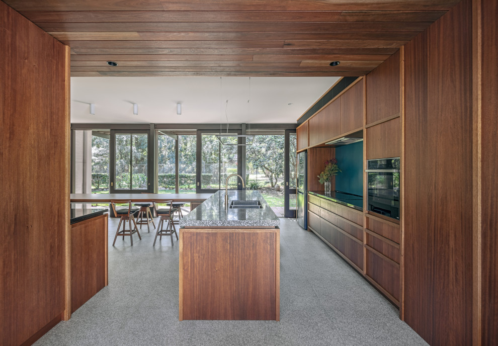 Photo of a midcentury l-shaped eat-in kitchen in Sydney with an undermount sink, flat-panel cabinets, medium wood cabinets, black appliances, with island, grey floor and grey benchtop.