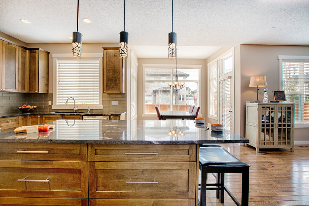 Eat-in kitchen - mid-sized rustic u-shaped medium tone wood floor and brown floor eat-in kitchen idea in Calgary with an undermount sink, shaker cabinets, medium tone wood cabinets, granite countertops, gray backsplash, glass tile backsplash, stainless steel appliances and an island