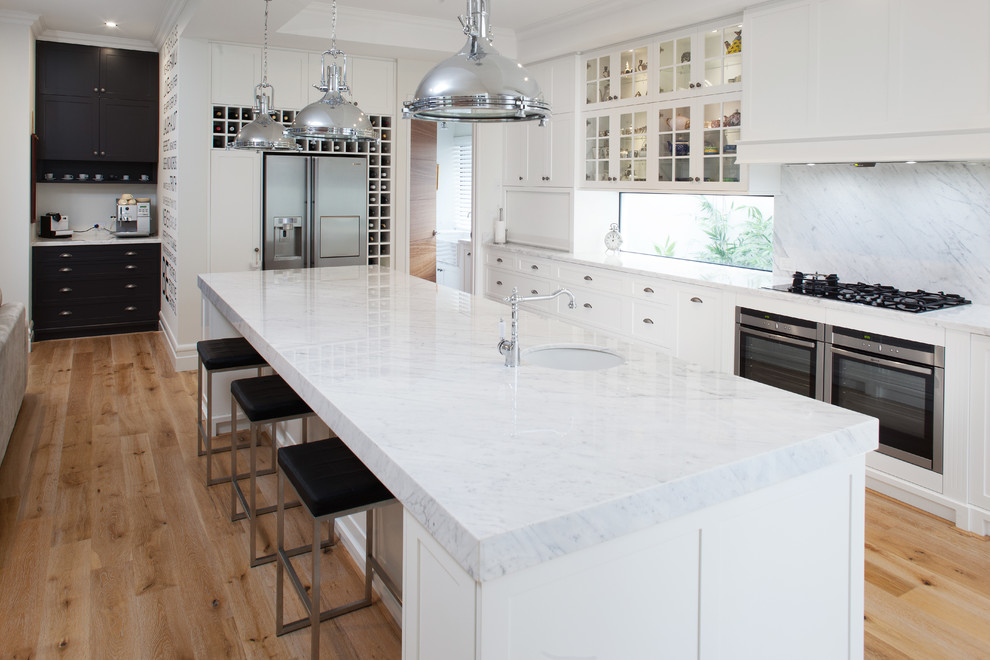 Large traditional kitchen in Perth with recessed-panel cabinets, white cabinets, marble benchtops, stone slab splashback, stainless steel appliances, with island, an undermount sink, grey splashback, grey benchtop and light hardwood floors.