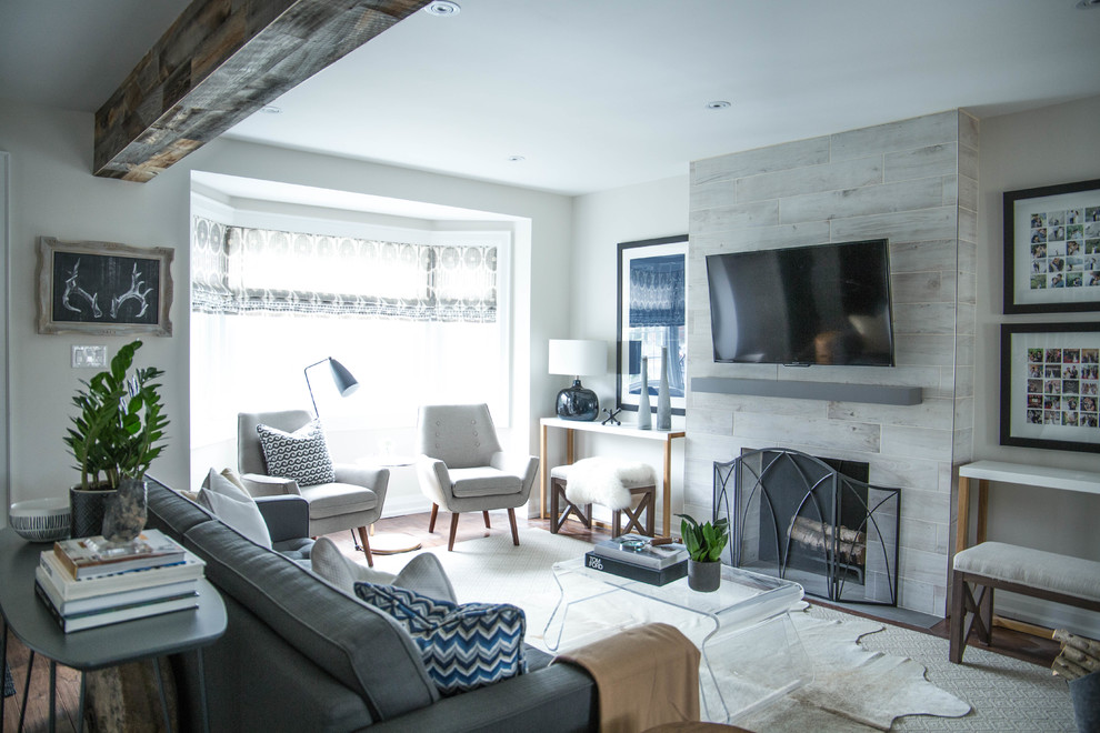 Inspiration for a small transitional open concept living room in Toronto with white walls, medium hardwood floors, a standard fireplace, a tile fireplace surround, a wall-mounted tv and brown floor.