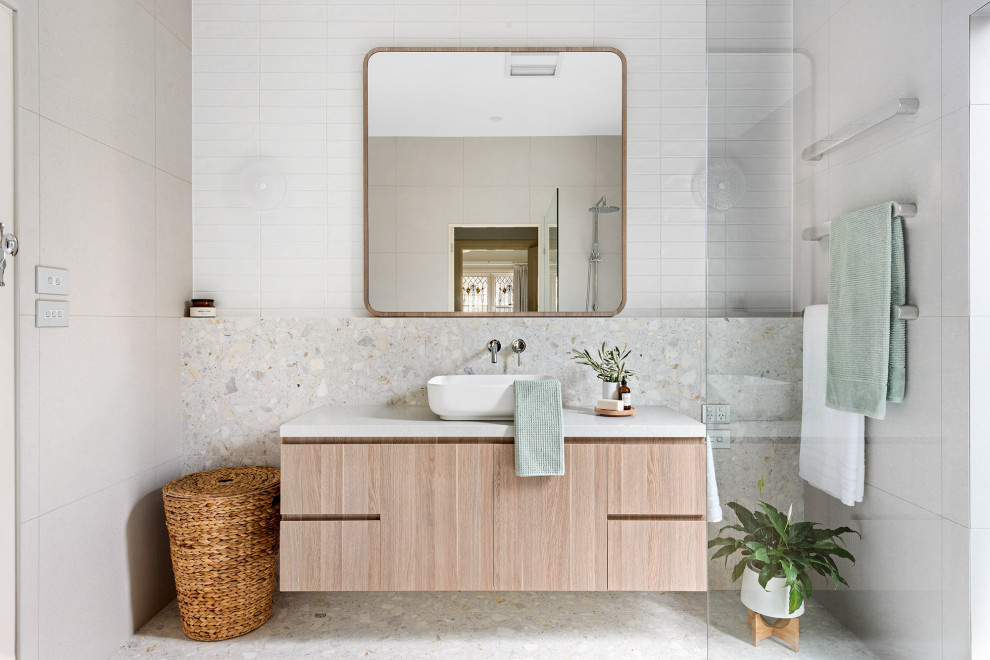 Photo of a mid-sized contemporary master bathroom in Melbourne with flat-panel cabinets, light wood cabinets, an open shower, a wall-mount toilet, gray tile, subway tile, grey walls, cement tiles, a vessel sink, limestone benchtops, grey floor, an open shower, white benchtops, a single vanity and a floating vanity.