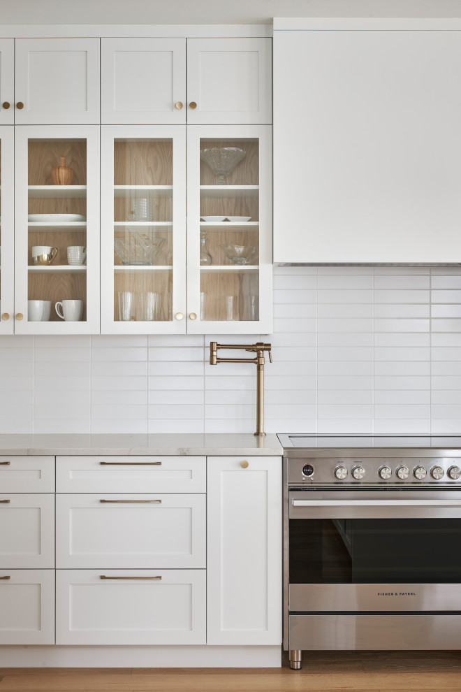 Inspiration for a transitional l-shaped light wood floor eat-in kitchen remodel in Ottawa with shaker cabinets, white cabinets, quartzite countertops, white backsplash, ceramic backsplash, paneled appliances and an island