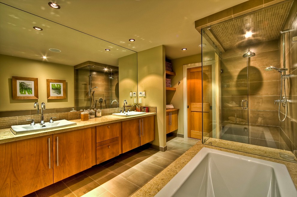 Photo of a large contemporary master bathroom in Vancouver with a drop-in sink, shaker cabinets, medium wood cabinets, limestone benchtops, a drop-in tub, a double shower, brown tile, porcelain tile, beige walls and porcelain floors.