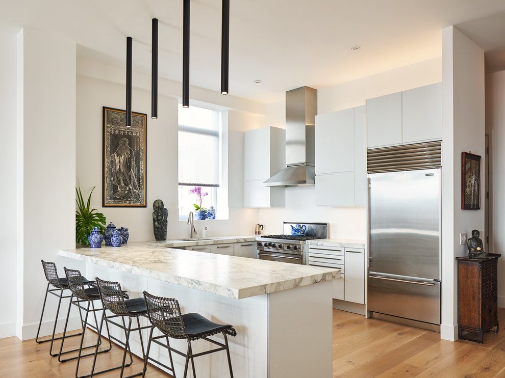 Asian u-shaped kitchen in New York with an undermount sink, flat-panel cabinets, white cabinets, white splashback, stainless steel appliances, light hardwood floors, a peninsula, beige floor and beige benchtop.