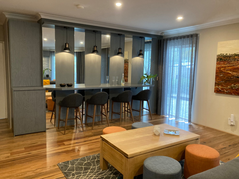 Design ideas for a mid-sized contemporary galley seated home bar in Perth with flat-panel cabinets, grey cabinets, laminate benchtops, mirror splashback, medium hardwood floors, brown floor and grey benchtop.
