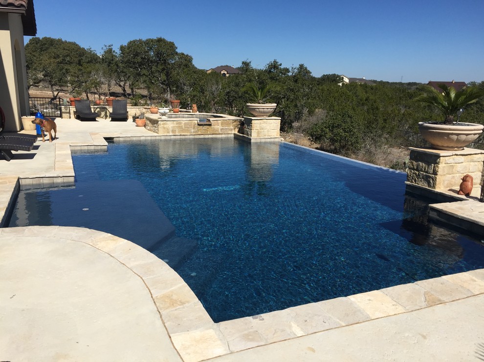 This is an example of a mid-sized modern backyard custom-shaped infinity pool in Austin with a water feature and decking.