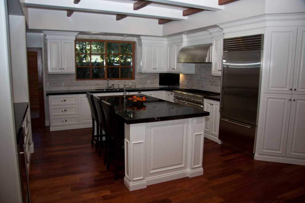 This is an example of a large traditional u-shaped eat-in kitchen in Orange County with an undermount sink, raised-panel cabinets, white cabinets, granite benchtops, beige splashback, travertine splashback, stainless steel appliances, medium hardwood floors, with island, red floor and black benchtop.