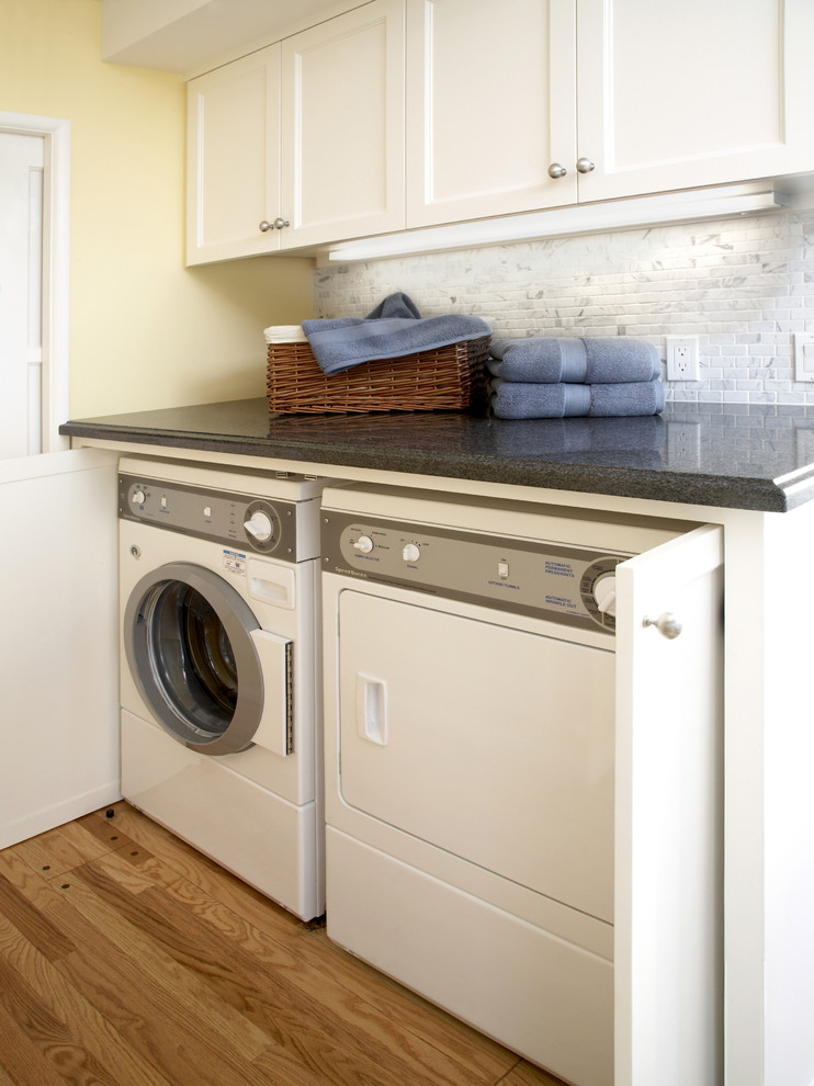 Mid-sized traditional laundry room in Los Angeles with shaker cabinets, white cabinets, granite benchtops, yellow walls, medium hardwood floors, a side-by-side washer and dryer, brown floor and grey benchtop.