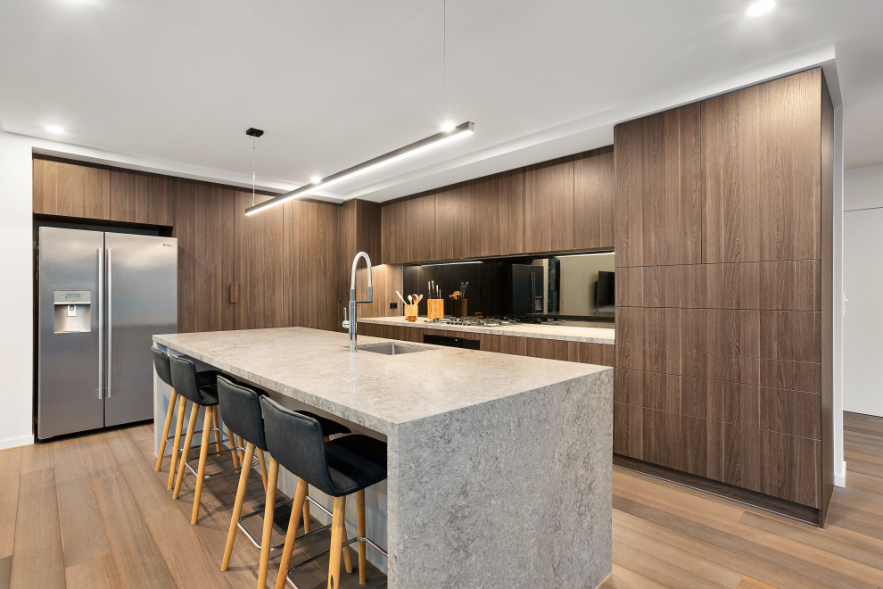 Inspiration for a contemporary l-shaped kitchen in Melbourne with an undermount sink, flat-panel cabinets, dark wood cabinets, mirror splashback, medium hardwood floors, with island, brown floor and grey benchtop.