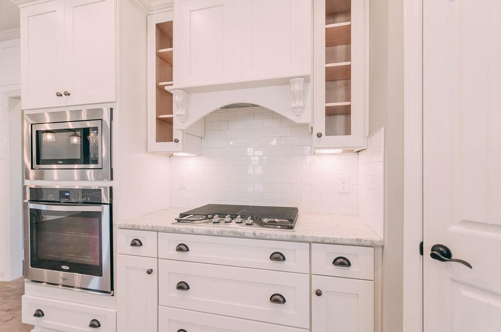 This is an example of a country l-shaped eat-in kitchen in Nashville with a farmhouse sink, recessed-panel cabinets, white cabinets, granite benchtops, white splashback, subway tile splashback, stainless steel appliances, medium hardwood floors and with island.