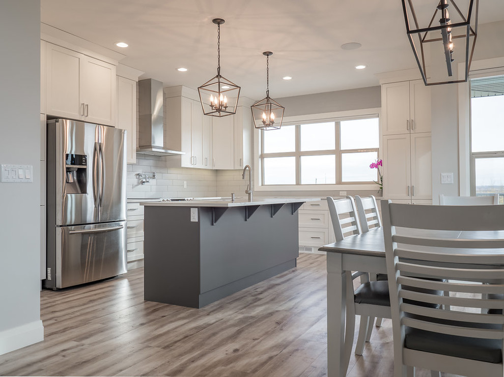 Mid-sized transitional l-shaped vinyl floor and brown floor eat-in kitchen photo in Edmonton with a double-bowl sink, recessed-panel cabinets, white cabinets, granite countertops, white backsplash, ceramic backsplash, stainless steel appliances and an island