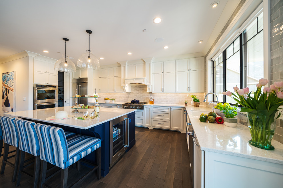 Foto på ett mellanstort maritimt grå kök, med en undermonterad diskho, luckor med infälld panel, blå skåp, bänkskiva i kvarts, grått stänkskydd, stänkskydd i keramik, rostfria vitvaror, mellanmörkt trägolv, en köksö och brunt golv