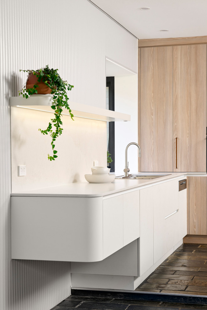 Photo of a large scandinavian l-shaped eat-in kitchen in Perth with a double-bowl sink, flat-panel cabinets, white cabinets, quartz benchtops, white splashback, engineered quartz splashback, black appliances, slate floors, with island, black floor and white benchtop.