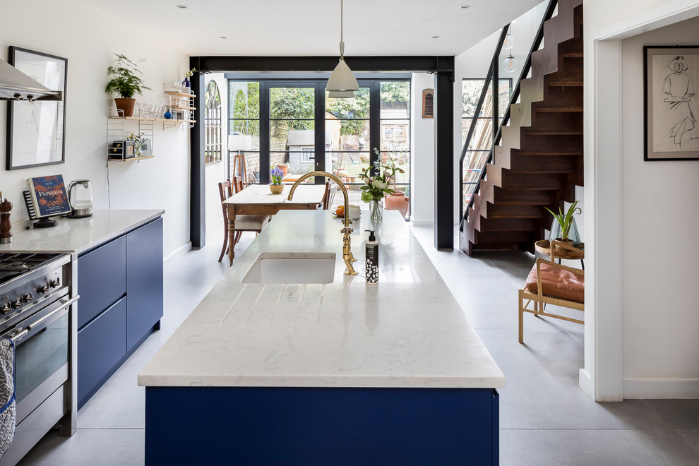 Photo of a large traditional single-wall kitchen pantry in London with a drop-in sink, recessed-panel cabinets, blue cabinets, granite benchtops, mirror splashback, stainless steel appliances, ceramic floors, with island and grey floor.