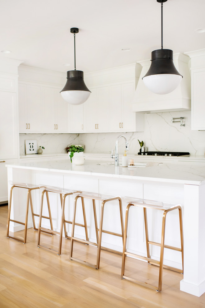 Inspiration for a transitional l-shaped eat-in kitchen in Cincinnati with an undermount sink, shaker cabinets, white cabinets, quartzite benchtops, white splashback, stone slab splashback, light hardwood floors, with island, white benchtop, panelled appliances and beige floor.