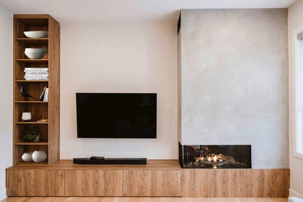 Cette photo montre un grand salon moderne ouvert avec un mur beige, parquet clair, une cheminée d'angle, un manteau de cheminée en béton et un téléviseur fixé au mur.