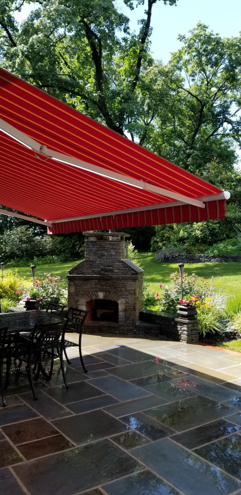 Large arts and crafts backyard patio in Philadelphia with natural stone pavers and an awning.