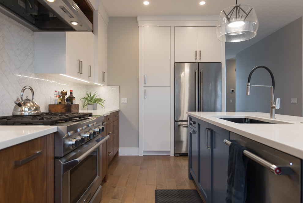 Example of a large transitional l-shaped light wood floor and brown floor eat-in kitchen design in Calgary with an undermount sink, flat-panel cabinets, white backsplash, stainless steel appliances, an island and white countertops
