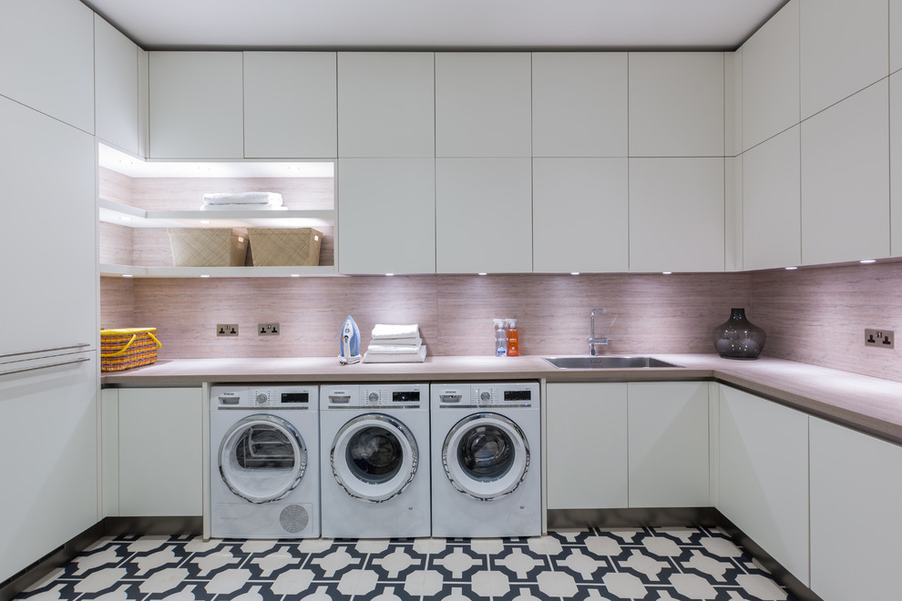 This is an example of a mid-sized contemporary u-shaped utility room in Gloucestershire with an integrated sink, flat-panel cabinets, white cabinets, laminate benchtops, white walls, porcelain floors, a side-by-side washer and dryer, multi-coloured floor and brown benchtop.