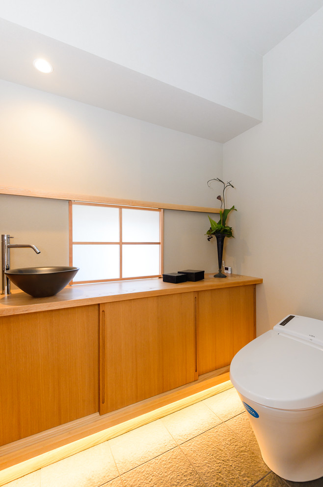 Inspiration for an asian powder room in Other with flat-panel cabinets, medium wood cabinets, white walls, a vessel sink, wood benchtops and brown benchtops.