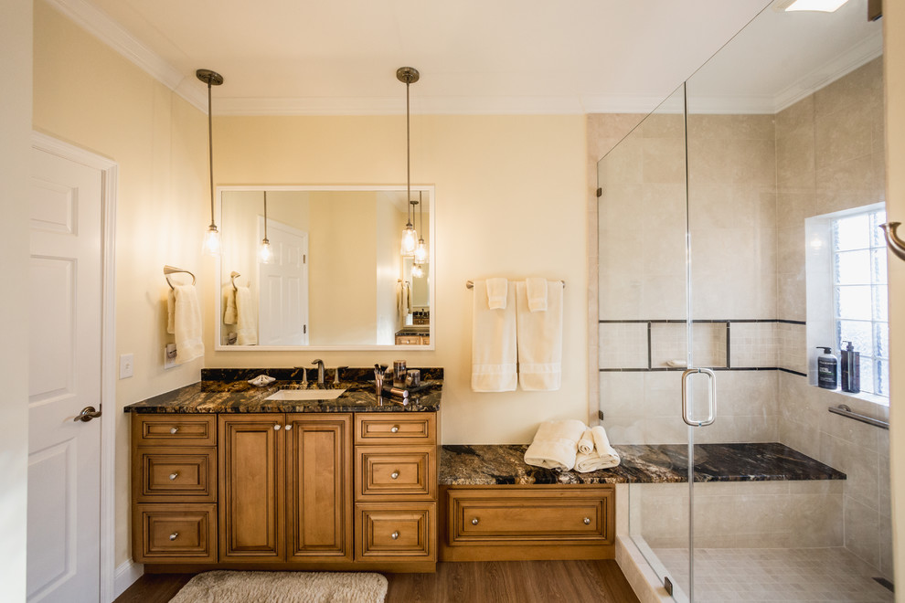 Large traditional master bathroom in Charleston with raised-panel cabinets, medium wood cabinets, an alcove shower, a one-piece toilet, beige tile, porcelain tile, black walls, laminate floors, an undermount sink, granite benchtops, brown floor and a hinged shower door.