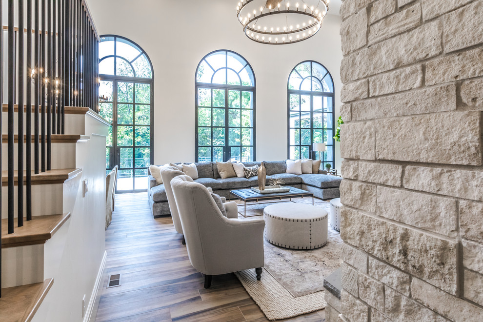 Photo of a large mediterranean open concept family room in Salt Lake City with beige walls, ceramic floors, a two-sided fireplace, a stone fireplace surround, a wall-mounted tv and brown floor.