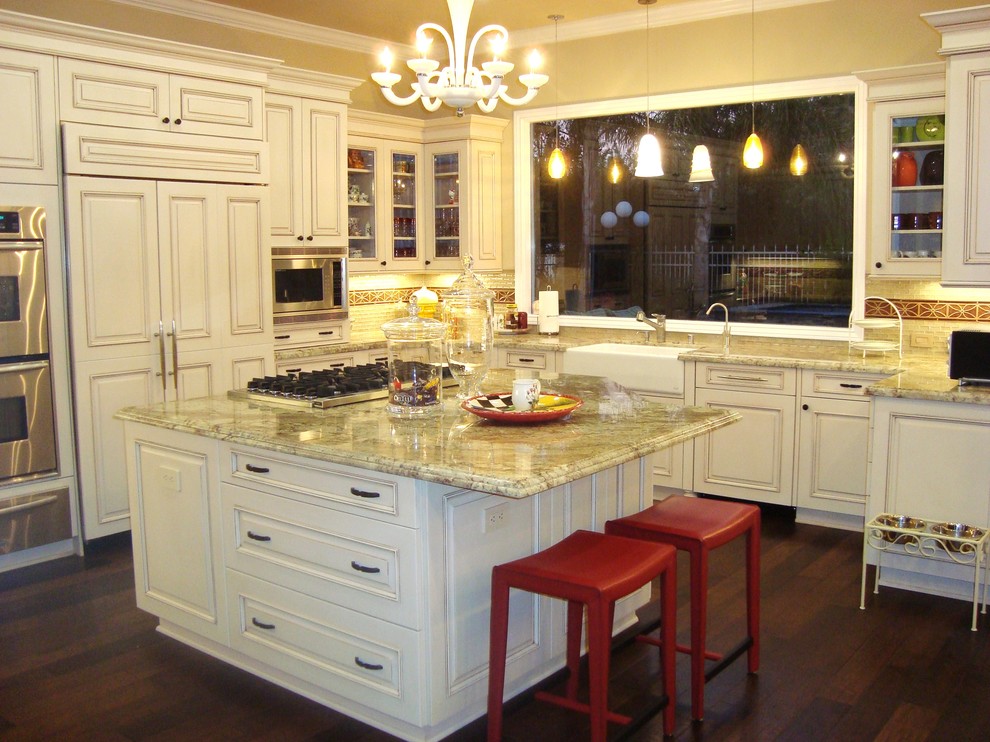 This is an example of a large traditional u-shaped eat-in kitchen in Los Angeles with raised-panel cabinets, white cabinets, beige splashback, dark hardwood floors, with island and panelled appliances.