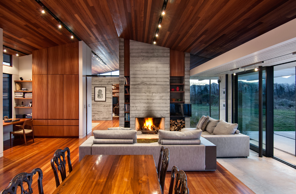 This is an example of a large contemporary open concept living room in Christchurch with medium hardwood floors, a standard fireplace, a concrete fireplace surround and no tv.